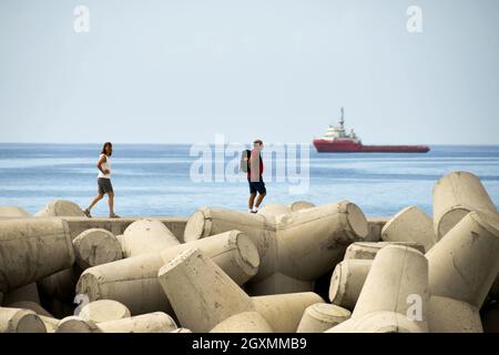 Funchal, Madeira, Portogallo - 2016 febbraio: Due persone che camminano sul muro di difesa del mare sul lungomare. La parete è costituita da forme in cemento pesante Foto Stock