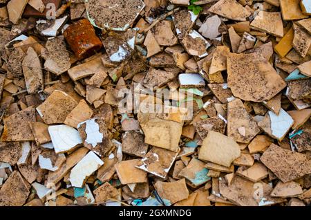 Sfondo di piastrelle rotte e dettaglio tubo arrugginito. Mattonelle rotte di beige chiaro e bianco poggiano a terra. Il concetto di distruzione, decadimento, detriti, env Foto Stock