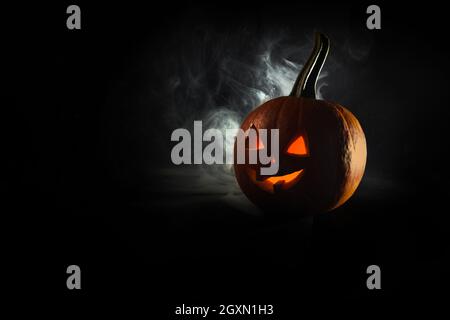 Halloween, zucca arancione con faccia luminosa su sfondo nero. Esce fumo denso. Foto Stock