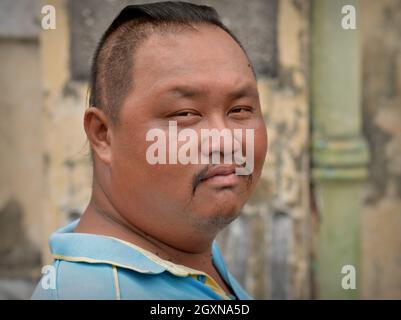 Camuffato chubby giovane malese cinese trishaw driver con baffi cinesi e moderni lati corti lungo taglio capelli guarda lo spettatore. Foto Stock