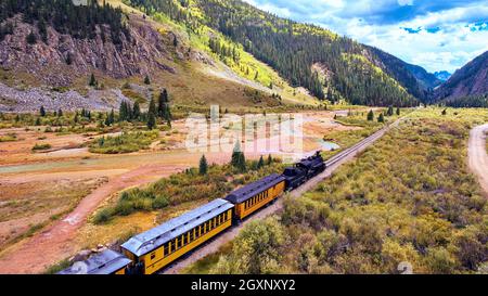 Vecchio treno nero con carbone che attraversa la valle circondata da montagne Foto Stock