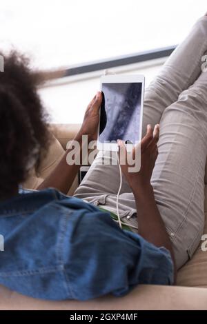 Giovani belle americano africano donna ama ascoltare la musica con le cuffie e tablet in poltrona nella sua casa di lusso Foto Stock