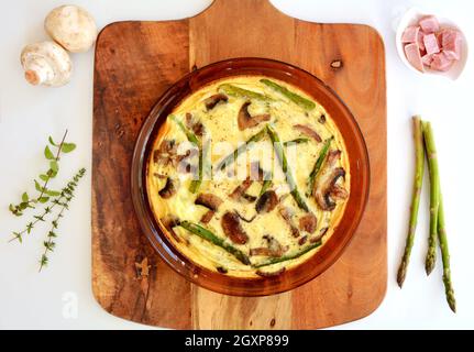 Prosciutto, funghi e asparagi frittata caldi dal forno in formato orizzontale sparato dall'alto. Cibo sano e nutriente per il comfort. Foto Stock