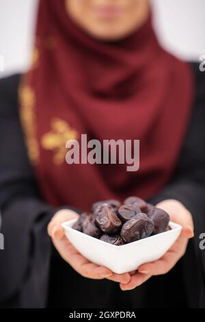 donna musulmana moderna che tiene un piatto pieno di datteri dolci sul tempo di iftar in ramadan kareem islamico sano concetto di cibo Foto Stock