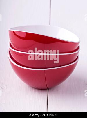 Svuotare il recipiente rosso per le insalate e tre tazze su un bianco tavolo di legno Foto Stock