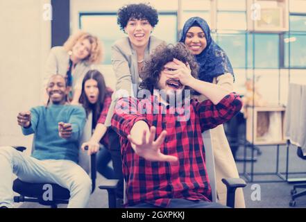 Multiethnics startup business team di sviluppatori di software per divertirsi durante la corsa su sedie da ufficio,entusiasti diversi dipendenti ridere godendo di un divertente Foto Stock