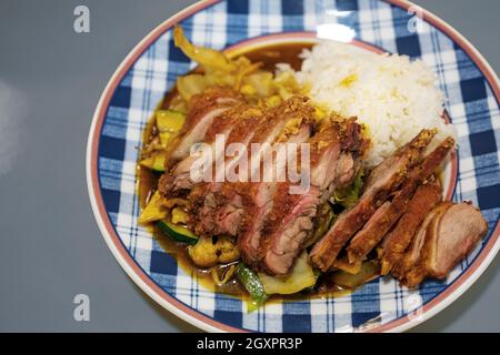 Pasto fritto croccante di anatra sulle verdure con riso su un piatto a motivi geometrici in un ristorante cinese di fast food, fuoco selezionato, profondità di campo stretta Foto Stock