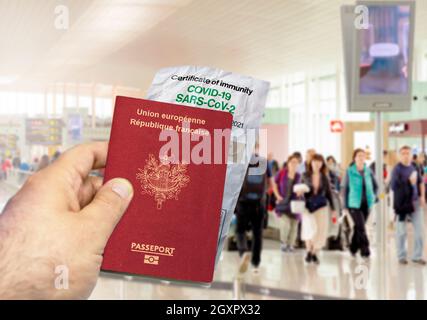 Mano che tiene un passaporto francese con un certificato di immunità Coronavirus Covid 19 di carta stropicciata. Aeroporto offuscato sullo sfondo. Immunità da Covid Foto Stock