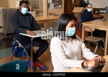 Istruzione scena in classe delle scuole superiori, studenti maschi e femmine si siedono in classe con computer portatili, ascoltando, indossando maschere per proteggere contro Covid-19 Foto Stock