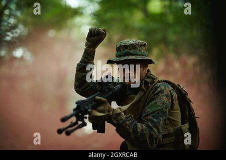 il soldato moderno della guerra sta mostrando i segnali tattici della mano per dare silenziosamente ordini e i generatori per l'ambiente della foresta della squadra Foto Stock