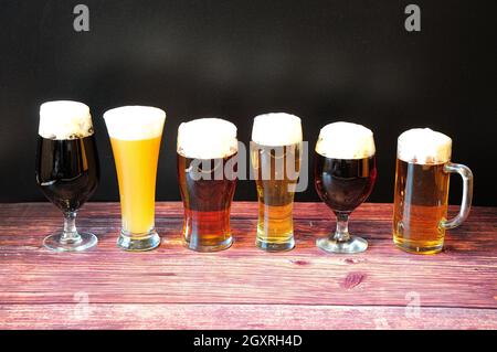 Sei diversi bicchieri di birra con sei diversi tipi di birra con stativo di schiuma in fila su un tavolo di legno. Primo piano. Foto Stock