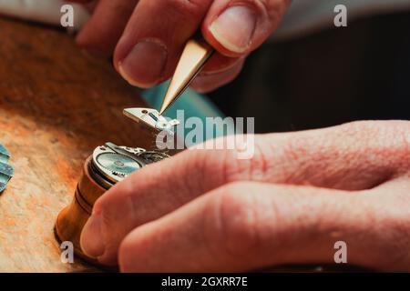 Orologiaio che lavora con il meccanismo a molla (a fuoco) di un vecchio orologio, tenendolo in un paio di pinzette durante la riparazione o la manutenzione dell'orologio Foto Stock