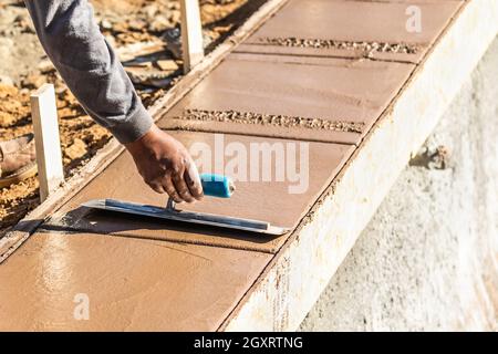 Lavoratore edile con frattazzo su cemento umida di coping di formazione intorno alla nuova piscina. Foto Stock