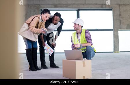 Ingegner architetto utilizzando computer portatile mentre mostra house design piani per una giovane coppia multietnica al sito in costruzione Foto Stock