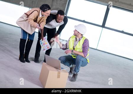 Ingegner architetto utilizzando computer portatile mentre mostra house design piani per una giovane coppia multietnica al sito in costruzione Foto Stock