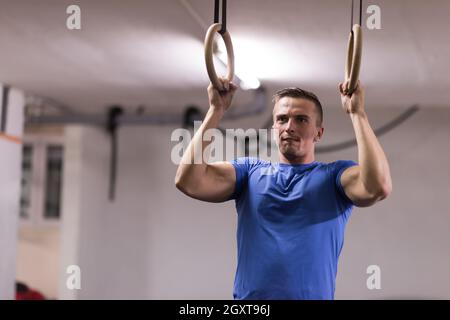 Fitness uomo bello fare immersione esercizio utilizzando anelli in palestra Foto Stock
