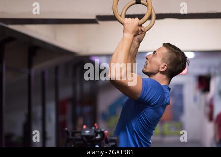 Fitness uomo bello fare immersione esercizio utilizzando anelli in palestra Foto Stock