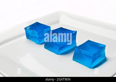 Quadrati blu di Jello ondulato su un piatto bianco su sfondo bianco Foto Stock