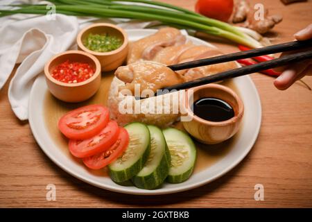 Mano ravvicinata con bacchette per bloccare il pollo in un piatto di riso Hainanese con deliziose salse e piatti vegetariani Foto Stock