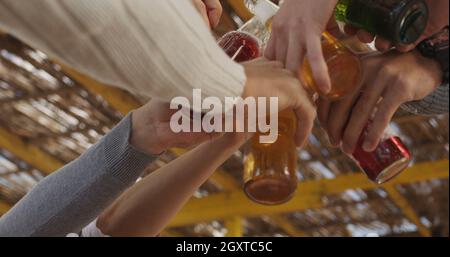 Giovani amici fare un brindisi con la birra e divertirsi intorno al falò presso il beach party sulla giornata autunnale Foto Stock