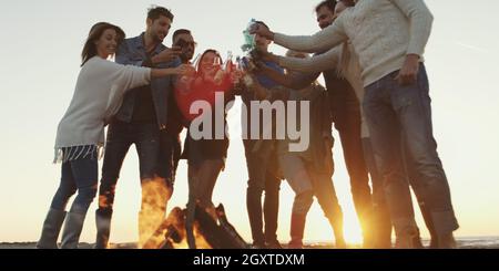 Giovani amici fare un brindisi con la birra e divertirsi intorno al falò presso il beach party sulla giornata autunnale Foto Stock