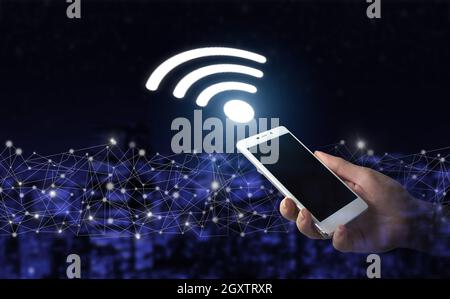 Concetto di connessione di rete aziendale e Wi-Fi in città. Smartphone bianco portatile con logo Wi Fi digitale ologramma su sfondo sfocato scuro della città. Foto Stock