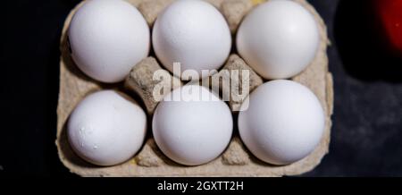 Sei uova bianche fresche in cartone sopra la superficie nera Foto Stock