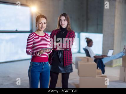 Due giovani donne d'affari allegre e casual con un collega afro-americano alle loro spalle che utilizzano un tablet sul cantiere durante il trasferimento in nuovi Foto Stock