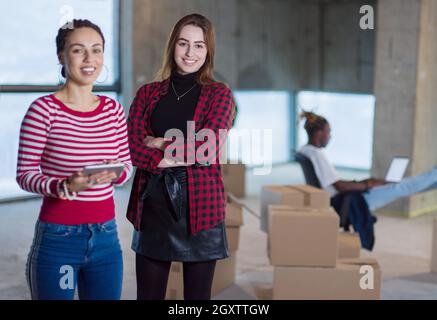 Due giovani donne d'affari allegre e casual con un collega afro-americano alle loro spalle che utilizzano un tablet sul cantiere durante il trasferimento in nuovi Foto Stock