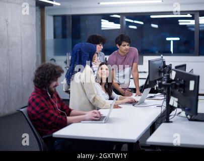 giovane team aziendale multietnico di sviluppatori di software che lavorano insieme utilizzando computer portatili e desktop mentre scrivono codice di programmazione presso il moderno Foto Stock