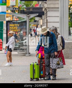 Coppia senior cammina su una strada della città di Vancouver con i tram di viaggio che voleranno via per le vacanze internazionali. BC, Canada-Agosto 15,2021 Foto Stock