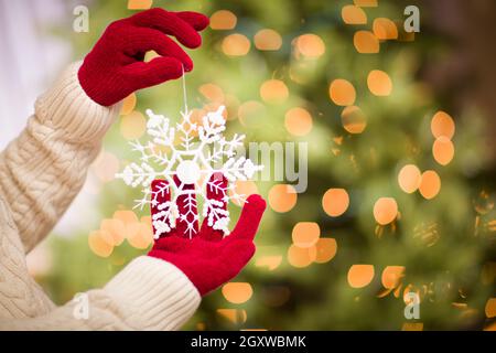 Donna che indossa rosso stagionale muffole tenendo premuto il simbolo del fiocco di neve bianca ornamento di Natale. Foto Stock