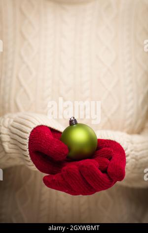 Donna che indossa rosso stagionale Mittens Holding Green ornamento di Natale. Foto Stock