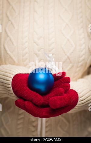 Donna che indossa stagionale muffole Rosso Blu Holding ornamento di Natale. Foto Stock