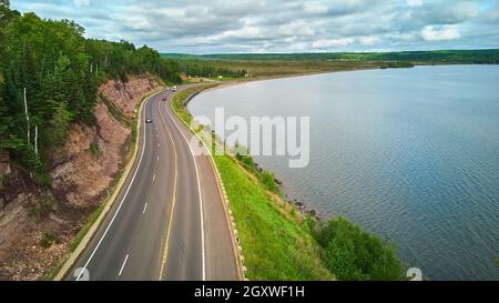 Vista aerea sulla strada intorno al grande lago contro le scogliere e la foresta lussureggiante Foto Stock