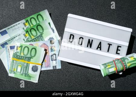 Lavagna luminosa con parola DONATE in lettere nere intorno alle banconote in euro. Denaro, imprese, finanza, investimenti, risparmio Foto Stock