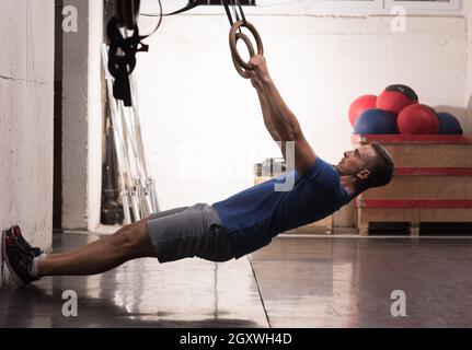 Fitness uomo bello fare immersione esercizio utilizzando anelli in palestra Foto Stock