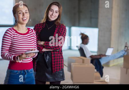 Due giovani donne d'affari allegre e casual con un collega afro-americano alle loro spalle che utilizzano un tablet sul cantiere durante il trasferimento in nuovi Foto Stock