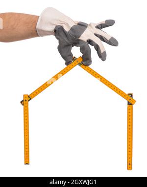Uomo a mano che indossa guanti da lavoro con misuratore di legno giallo a forma di casa. Attrezzo regolo di tenuta manuale, isolato su sfondo bianco. Foto Stock
