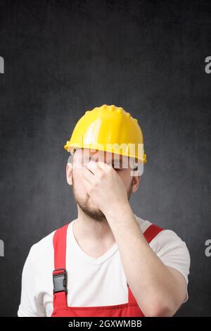 Stanco lavoratore edile in giallo elmetto, che copre il volto Foto Stock