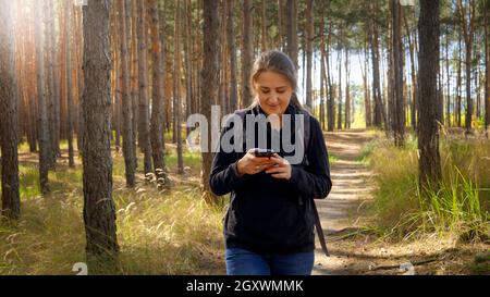 Ritratto di bella sorridente turista a piedi lungo il percorso escursionistico e utilizzando navigatore in smartphone. Foto Stock