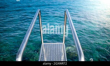 Corrimano e scala in metallo che conducono all'acqua limpida di mare turchese. Foto Stock