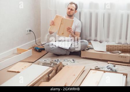 Uomo auto-assemblaggi mobili in legno a casa senza padrone. Leggere le istruzioni. Uomo che legge le istruzioni. Concetto DIY. Foto Stock