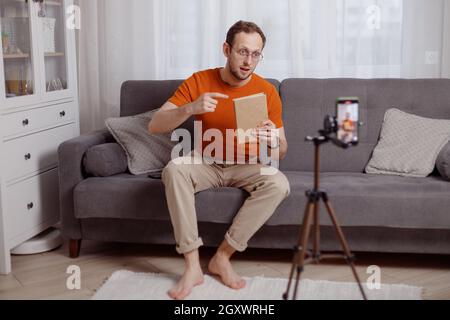 Bel blogger uomo a casa presenta libro mentre video stream. Social media marketing e vendite online. Foto Stock