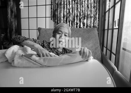 Una donna anziana con demenza seduta sul letto di allattamento giocando con una coperta Foto Stock