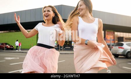 Ritratto di due ragazze allegre ridenti nello stesso vestito giocare e divertirsi sul parcheggio auto al centro commerciale. Foto Stock