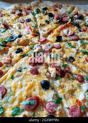 La pizza grande tagliata si trova sul primo piano del tavolo. Foto Stock