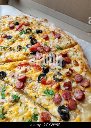 La pizza grande tagliata si trova sul primo piano del tavolo. Foto Stock