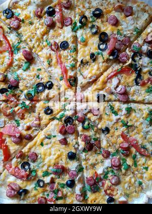 La pizza grande tagliata si trova sul primo piano del tavolo. Foto Stock