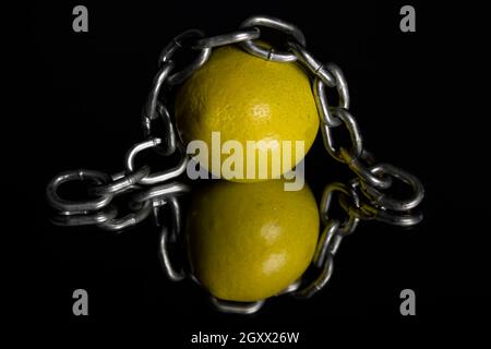 Una catena poggiante su un limone su uno sfondo riflettente nero lucido Foto Stock